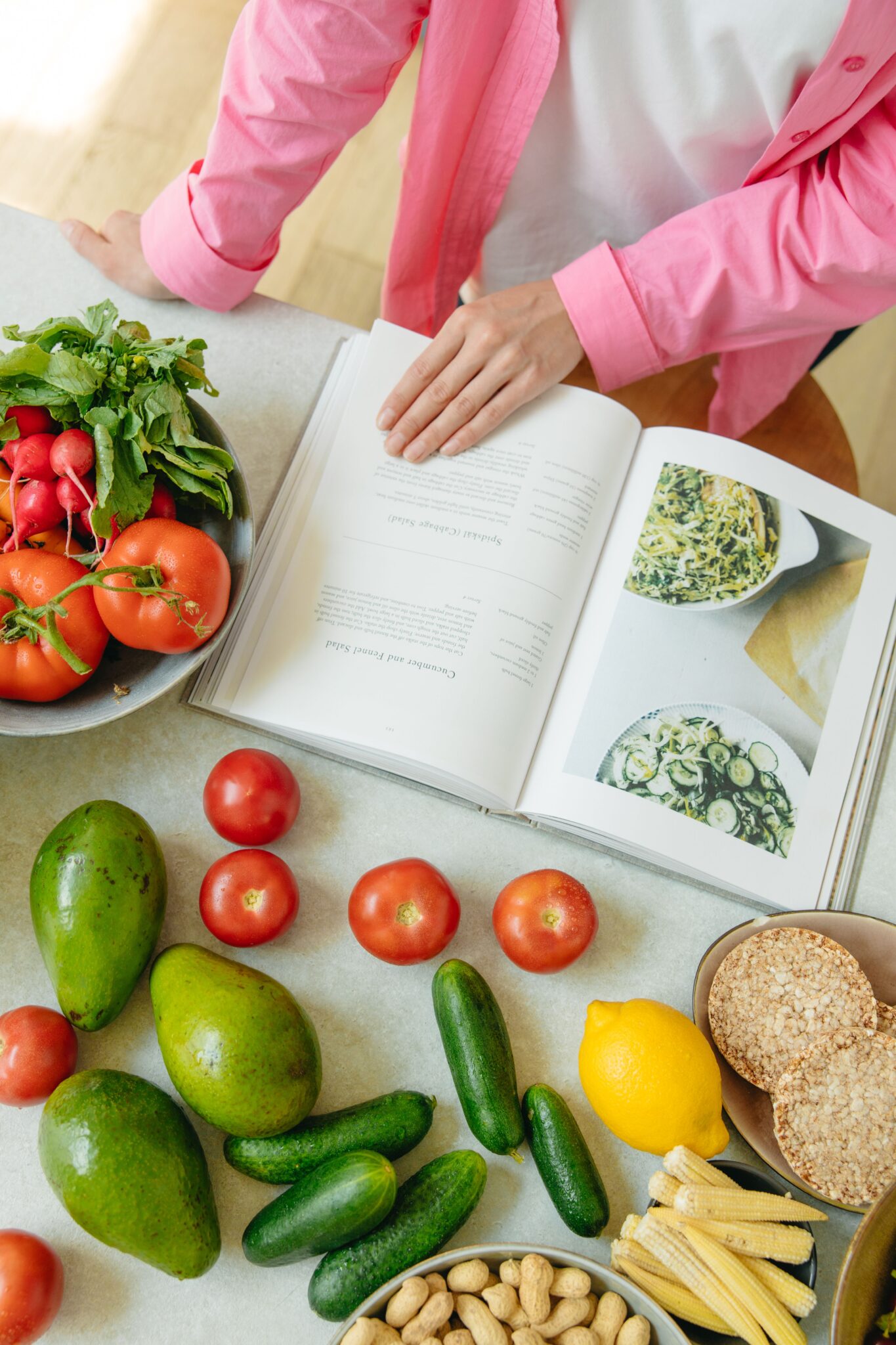 Persona consultando un libro de recetas de ensaladas junto a vegetales frescos